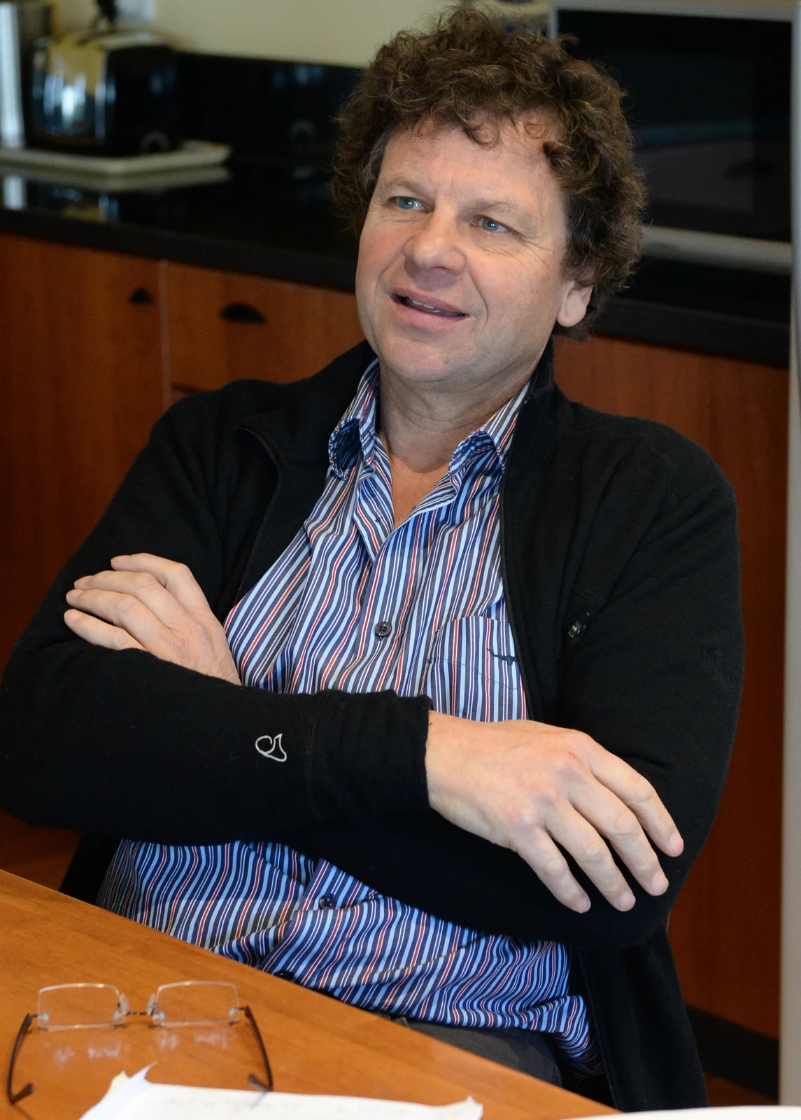Complete 2015 photograph of Simon McKeon seated with folded arms on the Mornington Peninsula, retaining the table, glasses and indoor surroundings.