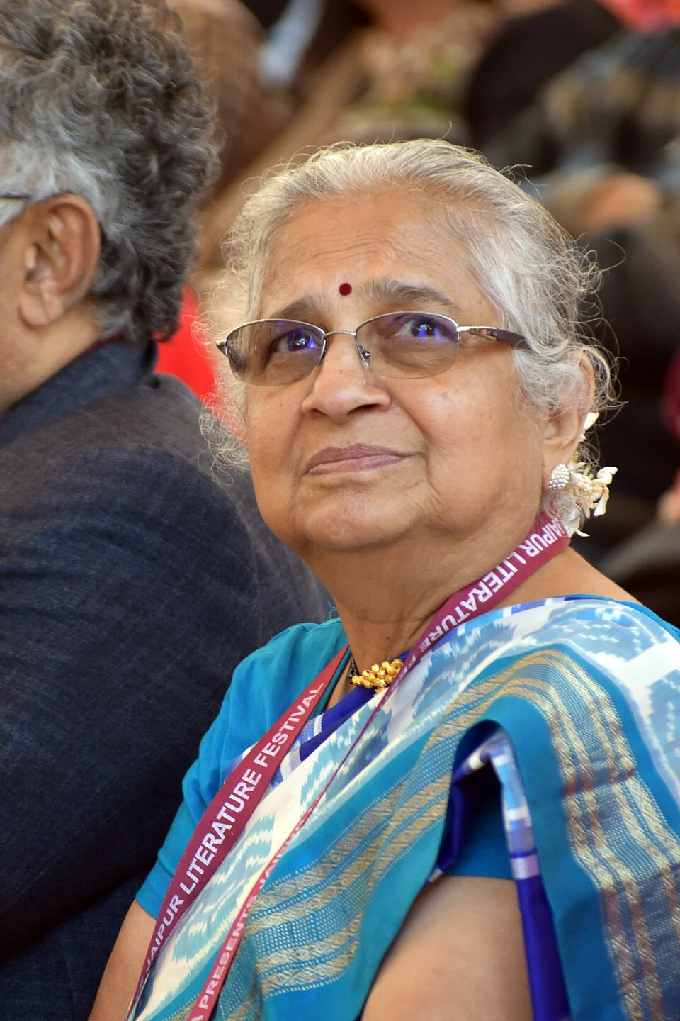 Sudha Murty in a blue sari at Jaipur Literature Festival in 2026, with the neighbouring attendee retained