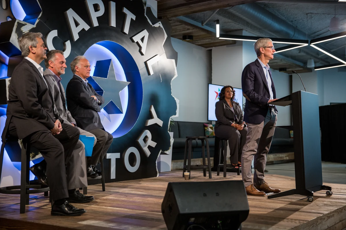 Tim Cook stands at a lectern at Capital Factory in Austin on 25 August 2017, with seated participants, the full stage, shoes, cables and foreground speaker retained.