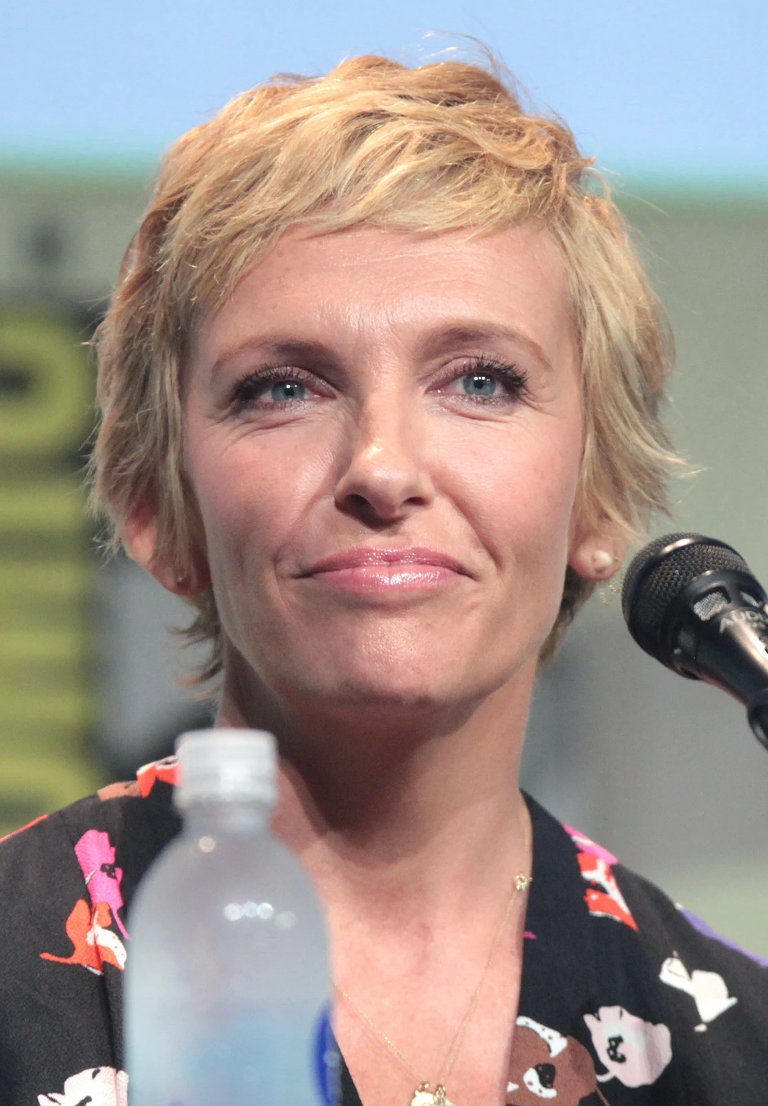 Toni Collette beside a microphone at the 2015 San Diego Comic-Con, with the complete supplied frame including the foreground bottle