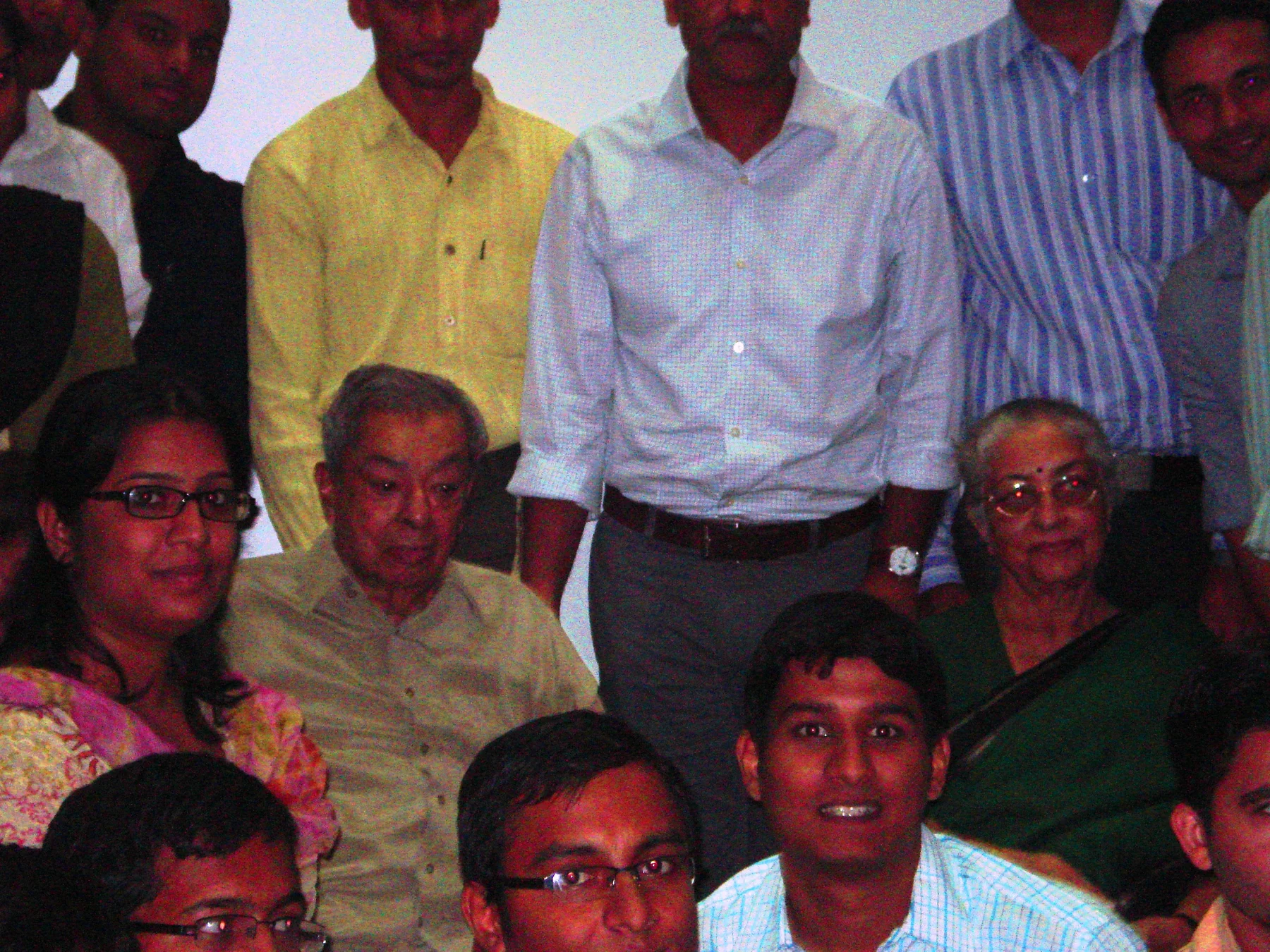 Verghese Kurien seated centre-left in a light shirt, surrounded by students in a dim group photograph.