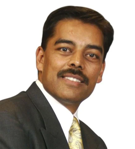 Vimal Shah in a dark jacket and yellow tie, smiling in the complete supplied portrait.
