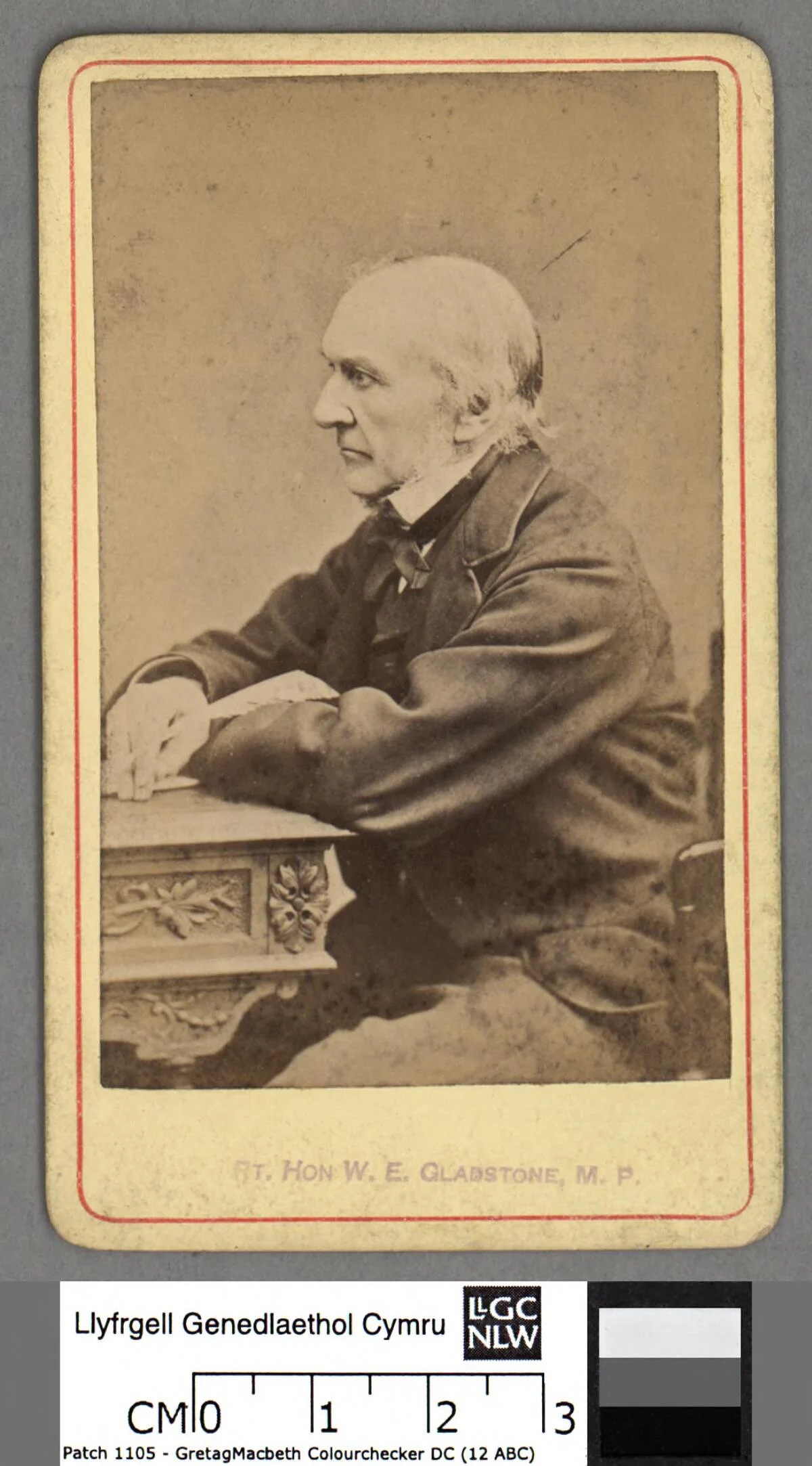 William Ewart Gladstone seated beside a table in a photograph dated circa 1860, with the complete mount and National Library of Wales catalogue scale.