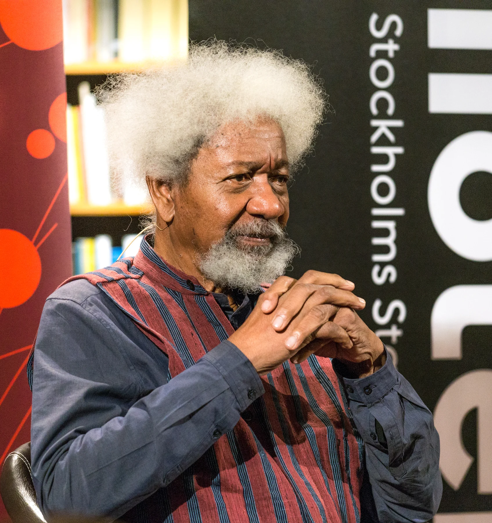Wole Soyinka seated with his hands together during a lecture at Stockholm Public Library in 2018.